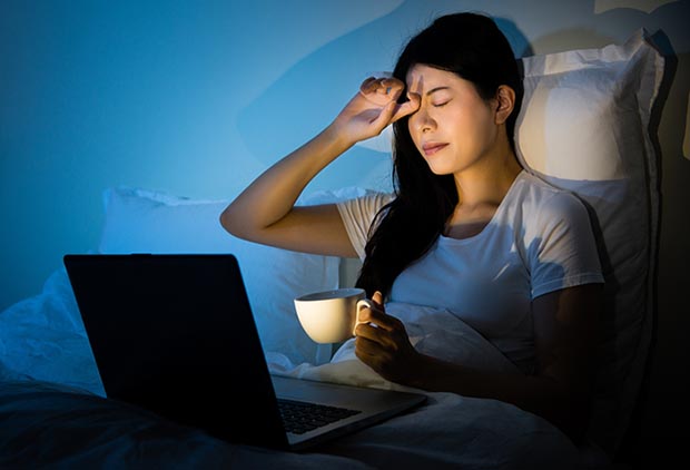 Woman in front of computer, grimacing with headache