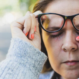 woman with glasses wiping eye
