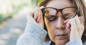 woman with glasses wiping eye